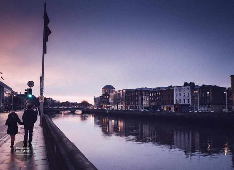A couple walk along the quays of Dublin as evening approaches